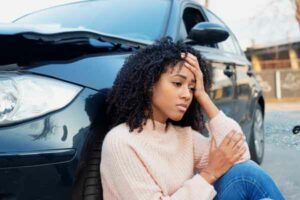 Woman sitting on ground leaning against car with hand on forehead Wrongful Death Lawyer Marietta GA